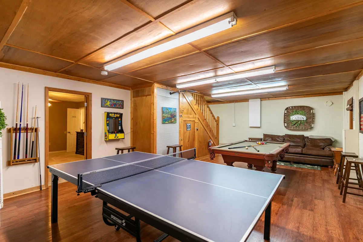 This image depicts a vibrant game room featuring both a pool table and a ping pong table, with a comfortable couch and bar stools nearby. The space is lively and designed for recreation, with plenty of room for group activities and friendly competitions.