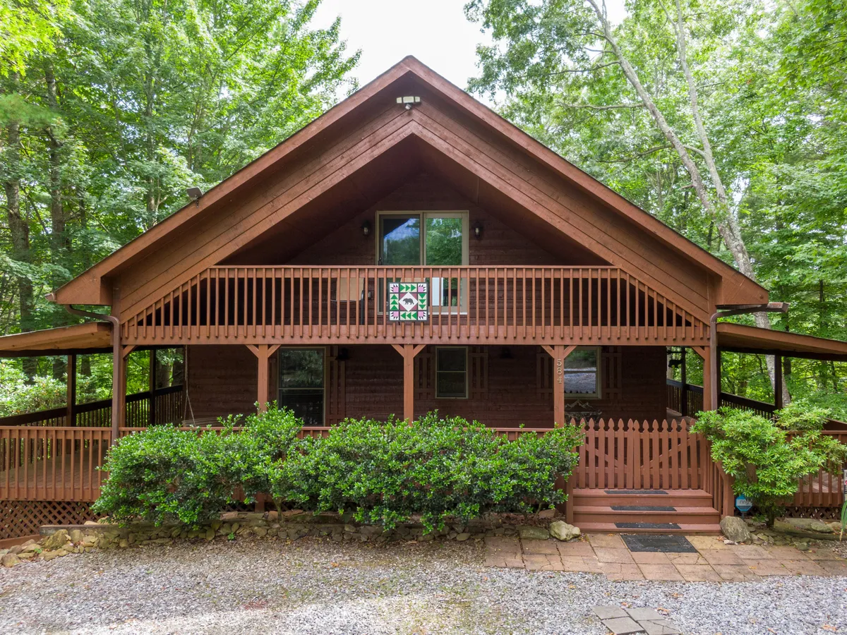 This image displays the cabin’s welcoming wooden porch framed by surrounding greenery, with a clear view of the front door and a decorative sign. The cozy porch setting invites guests to relax outdoors while being sheltered from the chilly winter air, offering a glimpse of the natural environment that surrounds the cabin.