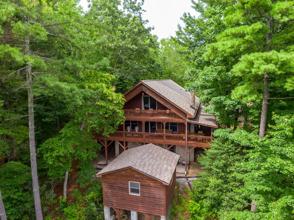 A wide wooden deck with large windows overlooks serene natural surroundings. The two-story structure creates a sense of openness and provides a versatile space for gatherings, outdoor meals, and restful moments with pets.