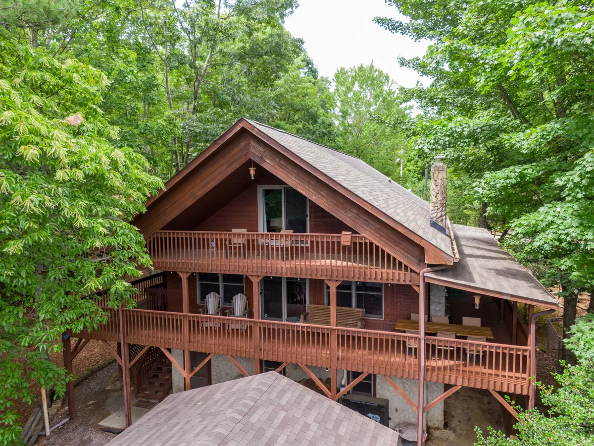 This image displays a welcoming wooden balcony featuring a sturdy stone chimney and large windows, set against a backdrop of lush natural surroundings. The balcony provides ample space for outdoor dining or relaxing, with panoramic views ideal for enjoying morning coffee or evening gatherings with friends and family.