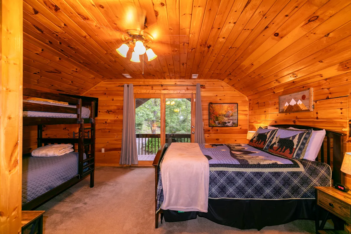 A spacious family suite with both a queen bed and bunk beds, wooden walls, large windows, and warm decorative touches. The room feels inviting and is designed for both adults and children to create lasting memories together.