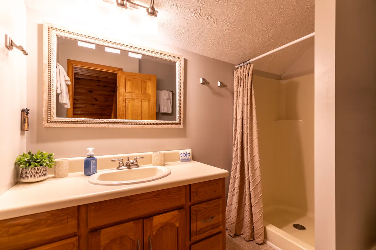A modern, spa-inspired bathroom with a large vanity sink, expansive mirror, wooden cabinetry, and a sleek shower area. The space exudes calm, making it perfect for a soothing start or end to the day.