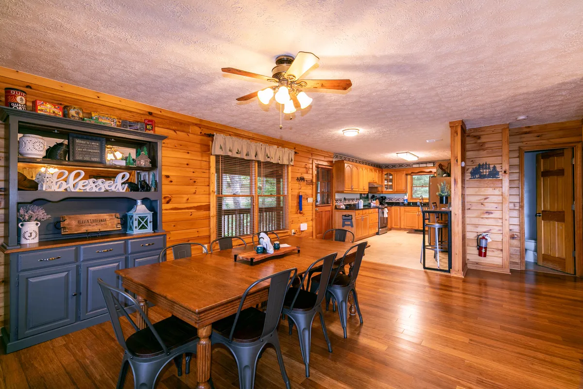 The dining area is showcased, featuring a large table that comfortably seats eight, with adjacent views of the kitchen and wooden cabinetry. The space is warmly lit and exudes a cozy, communal atmosphere ideal for group meals and memory-making.