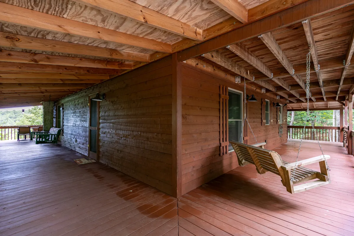 The photo captures a tranquil wooden swing on a spacious porch, flanked by robust beams and nestled within serene natural surroundings. The porch offers a peaceful retreat for enjoying a morning coffee, reading, or simply taking in the fresh mountain air and sunset views.