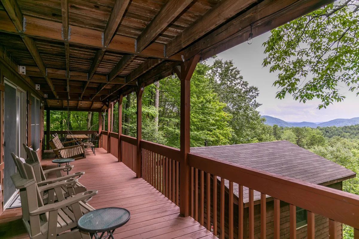 A peaceful covered deck with a seating area, surrounded by mountain views and natural beauty. The wooden deck invites guests to step outside, breathe in fresh air, and enjoy the tranquil setting.