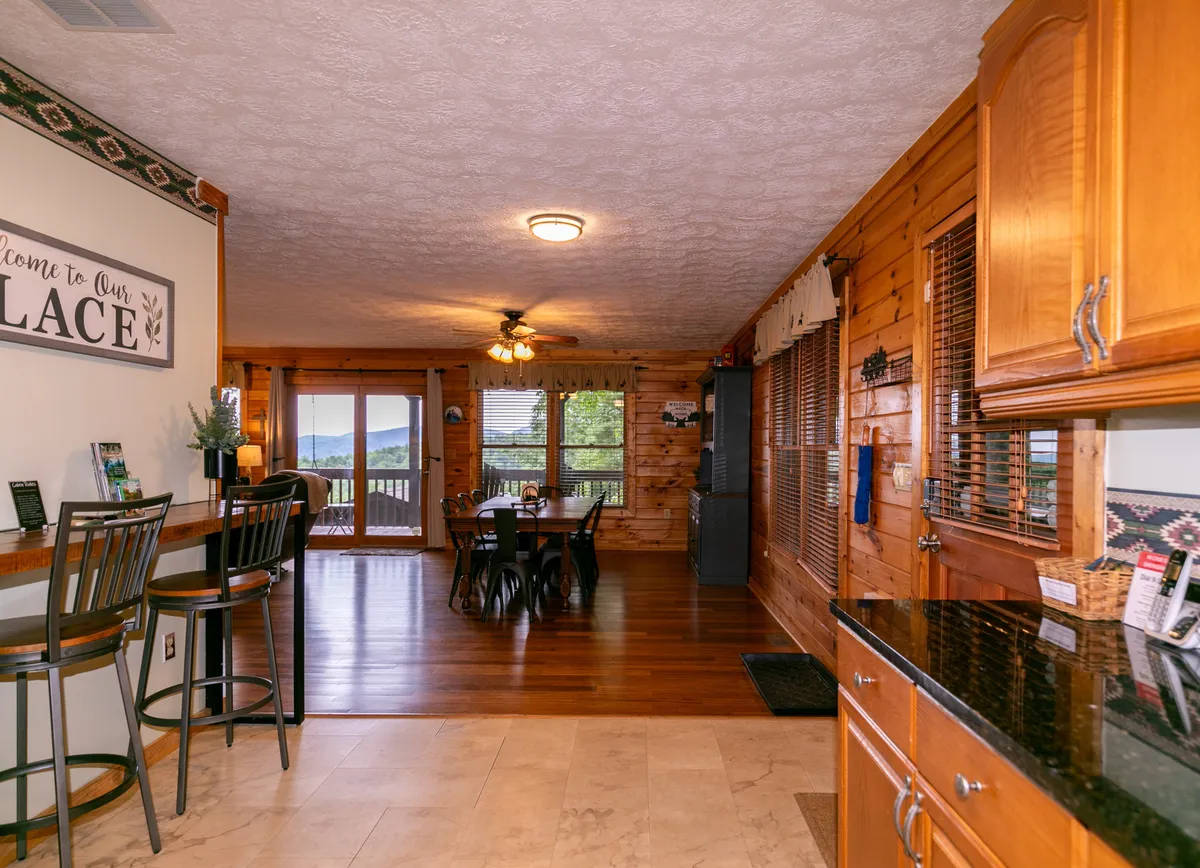 A harmonious blend of the dining table, bar stools at the breakfast bar, and large windows that let in natural light. The "welcome" sign adds a personal touch, emphasizing the space’s inviting feel and the connection between the kitchen and dining areas.
