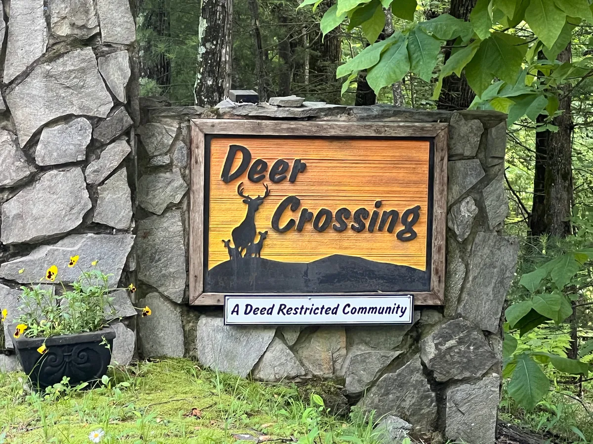 An exterior shot featuring a stone structure, a 'Deer Crossing' sign, and a flower planter, all set in a serene, natural landscape. This scene evokes the sense of arriving at a mountain getaway where nature and rustic charm abound, and hints at the wildlife and community spirit of the area.