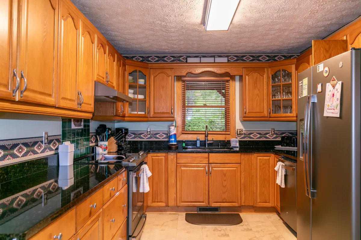 This image highlights the kitchen's granite countertops, wood cabinetry, and stainless steel appliances, with a window allowing natural light to pour in. The countertops are spacious and inviting, perfect for meal preparation or gathering around for shared cooking experiences.